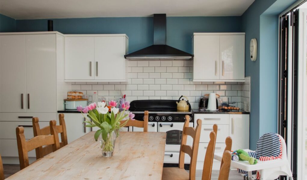 A vase of tuplips sat on a rectangular table in a kitchen. The Kitchen has blue walls and white units