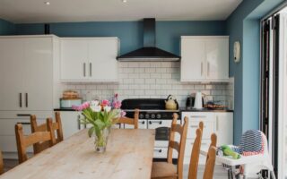 A vase of tuplips sat on a rectangular table in a kitchen. The Kitchen has blue walls and white units