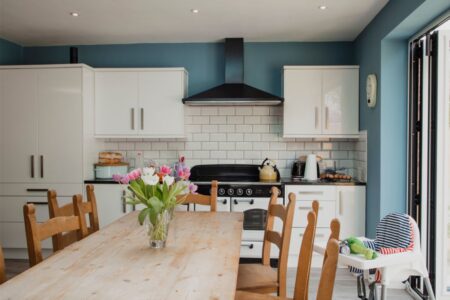 A vase of tuplips sat on a rectangular table in a kitchen. The Kitchen has blue walls and white units